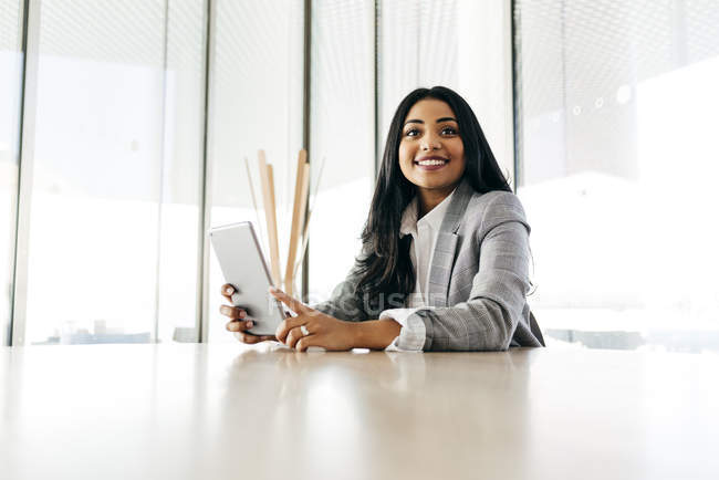 Portrait of smiling businesswoman with tablet sitting at table and looking aside — Stock Photo