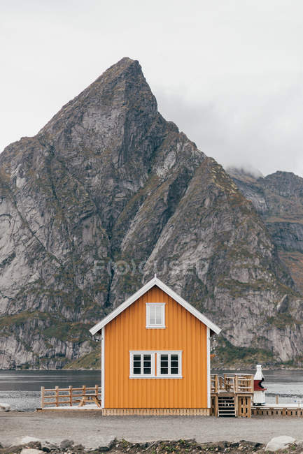 Cabin on lake shore over Mountain cliff on background — Stock Photo