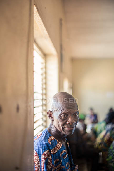 BENIN, ÁFRICA - AGOSTO 31, 2017: Retrato de homem idoso de camisa colorida posando pelo peitoril da janela e olhando para longe . — Fotografia de Stock