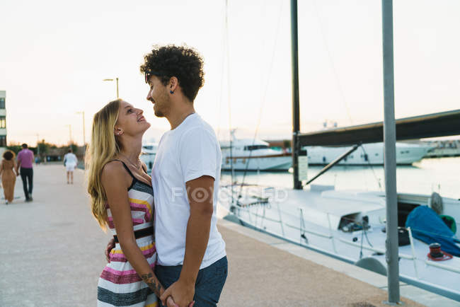 Вид збоку щасливої пари, що обіймається пірсом з швартованими яхтами — стокове фото