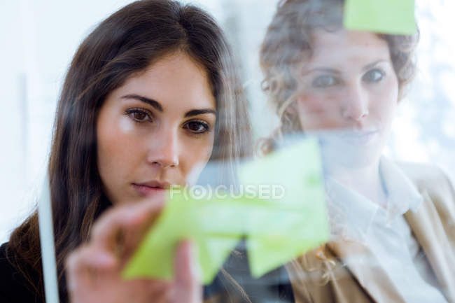 Retrato de mujer de negocios pegando nota sobre vidrio en la oficina
. - foto de stock