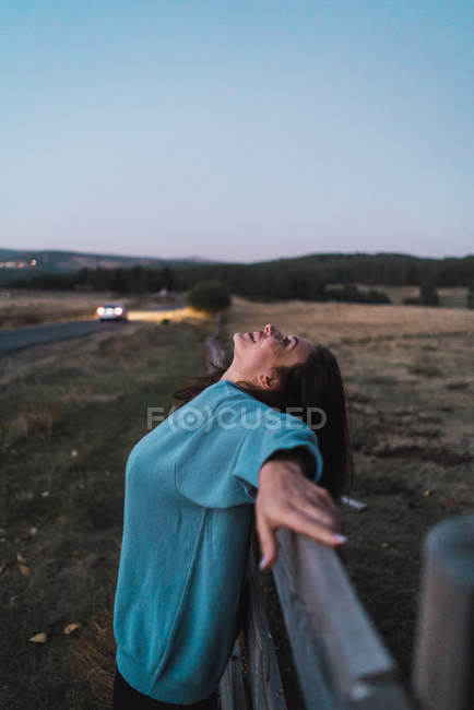 Vista laterale ragazza in felpa blu seducente appoggiata sulla recinzione in campagna — Foto stock