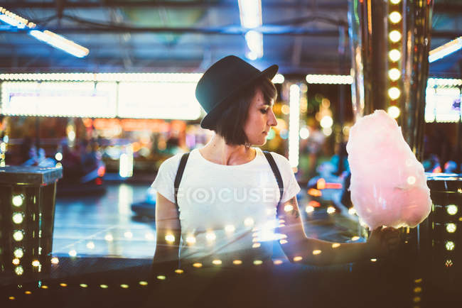 Вид збоку молода жінка тримає рожевий цукрова вата і позують романтично у вогні парк розваг. — стокове фото