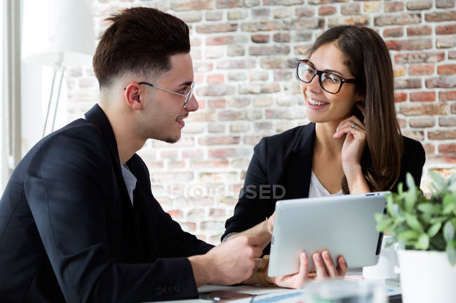 Portrait of business people using tablet and looking at each other in modern office. — Stock Photo