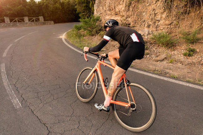 Задний вид велосипедиста на велосипеде вдоль асфальтовой дороги возле глиняной скалы в солнечный день . — стоковое фото