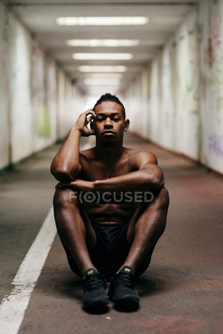 Shirtless sportsman sitting on floor at underground passage — Stock Photo