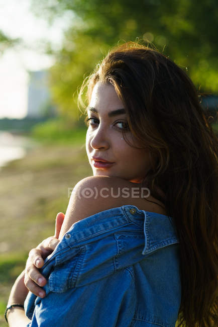 Attractive woman taking off denim shirt and looking over shoulder at camera — Stock Photo