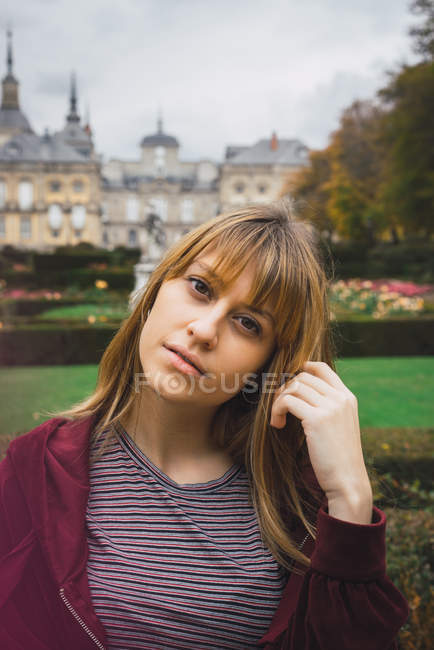 Bella ragazza bruna guardando la fotocamera sopra la villa e il giardino sullo sfondo — Foto stock