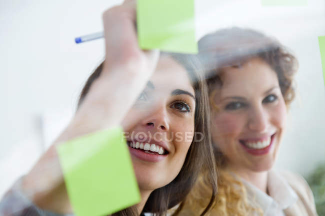 Portrait of smiling business woman making note on sticker at glass wall. — Stock Photo