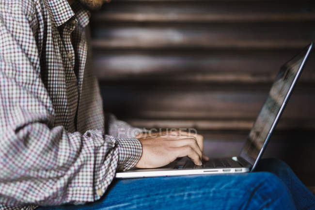Mid section of man sitting staircase with laptop on knees and typing — Stock Photo