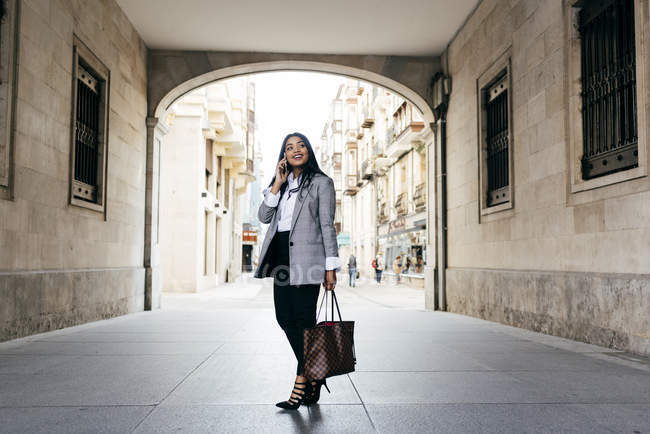Élégante femme d'affaires souriante avec téléphone posant à l'arche de la rue — Photo de stock