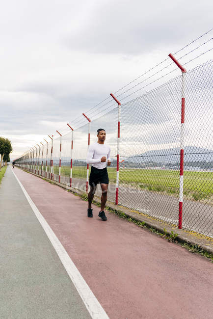 Frontansicht eines Mannes, der am Zaun entlangläuft — Stockfoto