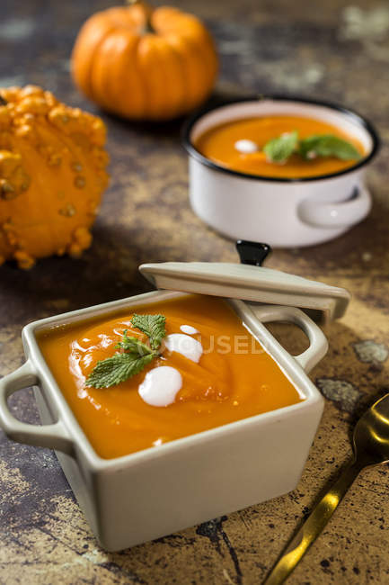 Cream of pumpkin in square ceramic sauce pot on stone surface — Stock Photo