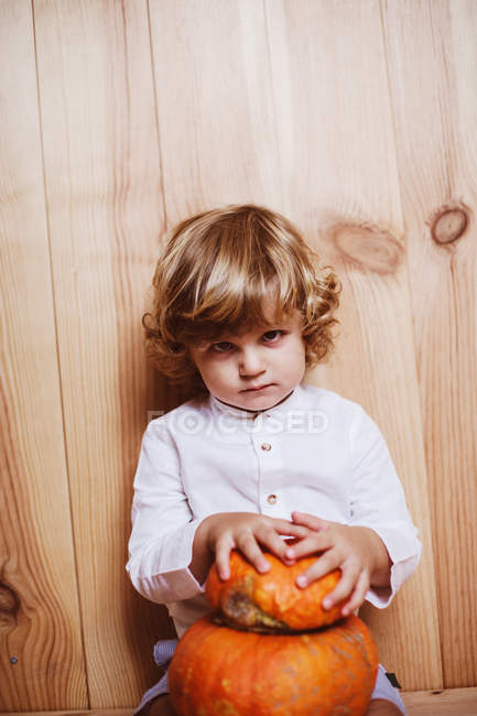 Confident boy posing with pumpkin by wooden wall — Stock Photo