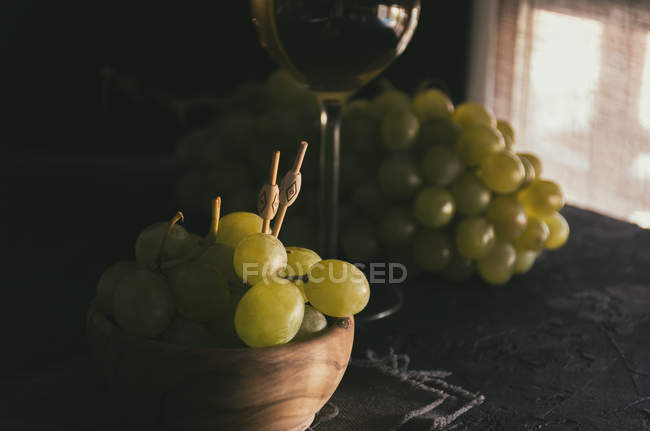 Close up view of bunch of green grapes with skewers in bowl beside glass of white wine — Stock Photo