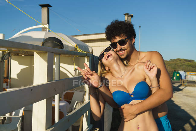 Portrait of man embracing laughing girlfriend in swim suit at beach — Stock Photo