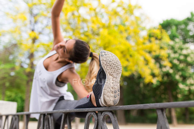 Chica bonita estirando el cuerpo con la pierna en la valla del parque - foto de stock
