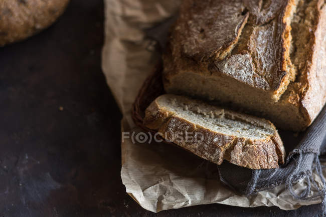 Vista superior de pan casero y rebanada en papel rústico - foto de stock