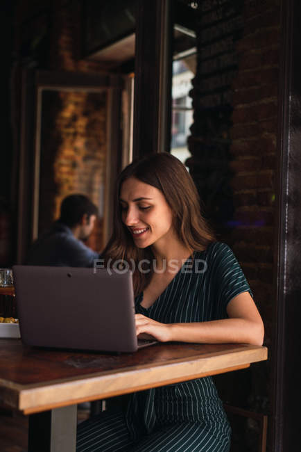 Retrato de la mujer bonita usando el ordenador portátil en la cafetería de la ciudad - foto de stock