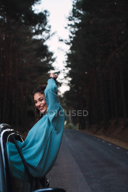 Sorrindo mulher inclinando-se para fora janela do carro durante a viagem através da floresta . — Fotografia de Stock