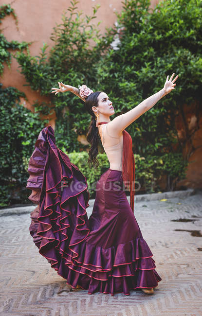 Vista lateral do dançarino de flamenco vestindo traje típico posando sobre planta abraçada parede de rua — Fotografia de Stock