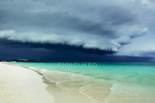 Пейзаж білого піщаного пляжу та бірюзової океанічної води під грозовою темною хмарою . — стокове фото