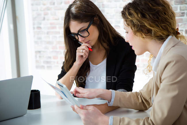 Ritratto di due imprenditrici che utilizzano tablet digitale mentre discutono in ufficio . — Foto stock