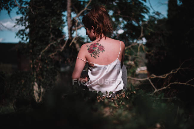 Visão traseira da morena com tatuagem nas costas cutucando na floresta — Fotografia de Stock