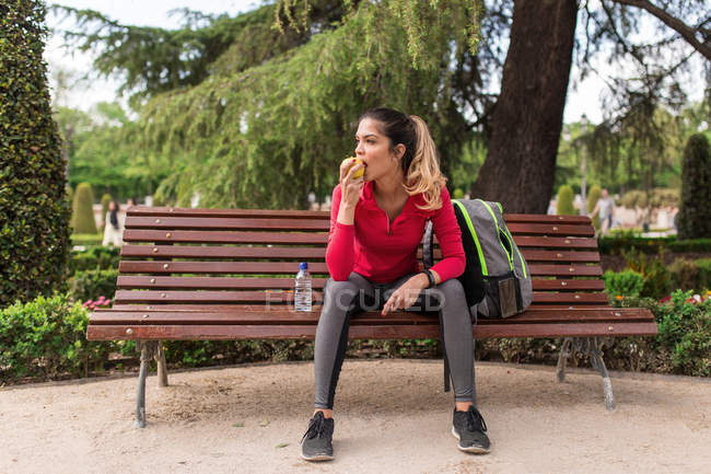 Спортивная женщина сидит на скамейке в ковчеге и ест яблоко — стоковое фото