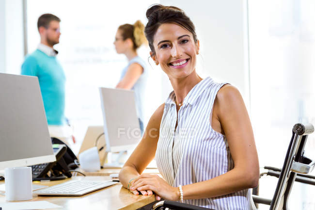 Портрет улыбающейся деловой женщины, сидящей за столом в офисе и смотрящей в камеру  . — стоковое фото