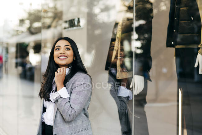Mujer alegre con chaqueta elegante posando cerca del escaparate - foto de stock