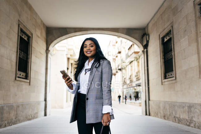 Elegant smiling businesswoman posing with phone at archway — Stock Photo