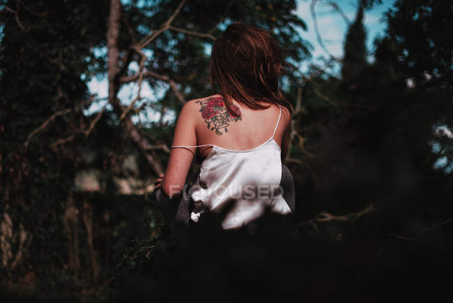 Вид ззаду дівчини з татуюванням на плечі, що йде в саду — стокове фото