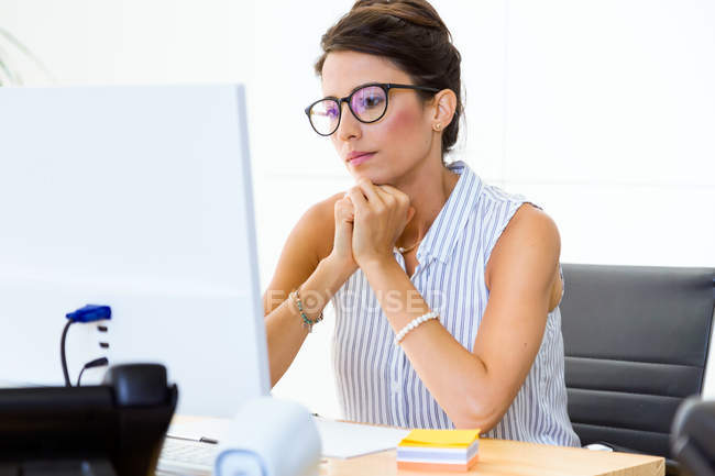 Porträt einer Geschäftsfrau, die am Arbeitsplatz sitzt und auf den Monitor blickt — Stockfoto