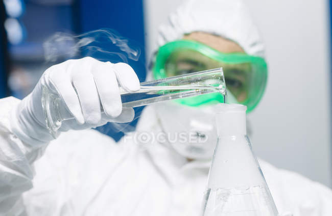 Científico vertiendo líquido en un matraz humeante - foto de stock