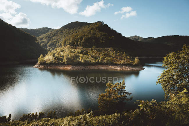 Paesaggio di lago in bacino di montagne verdi con cielo azzurro che riflette in acqua . — Foto stock