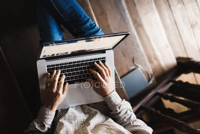 Земледелец сидит на лестнице с ноутбуком на коленях и печатает — стоковое фото