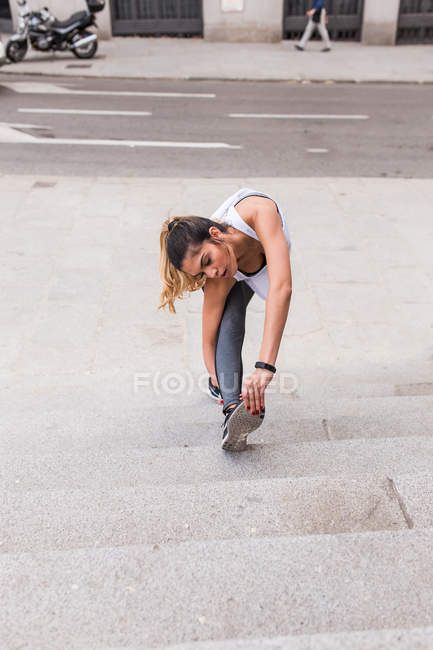 Vista frontale della donna sportiva che si estende fino gamba alle scale — Foto stock