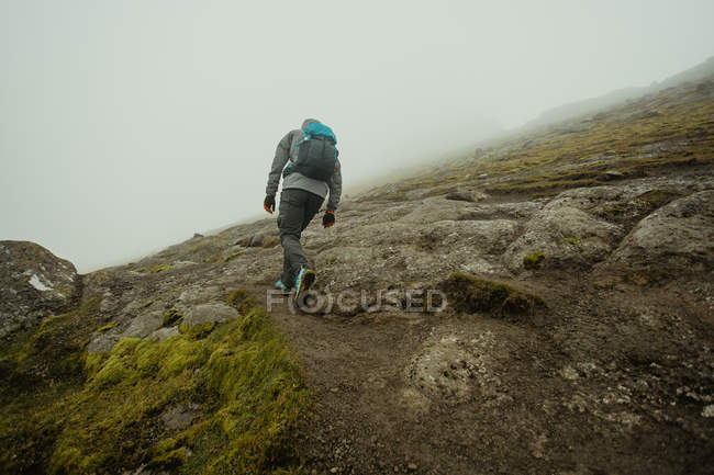 Rear view of man walking up rocky moss-covered slope of hill — Stock Photo
