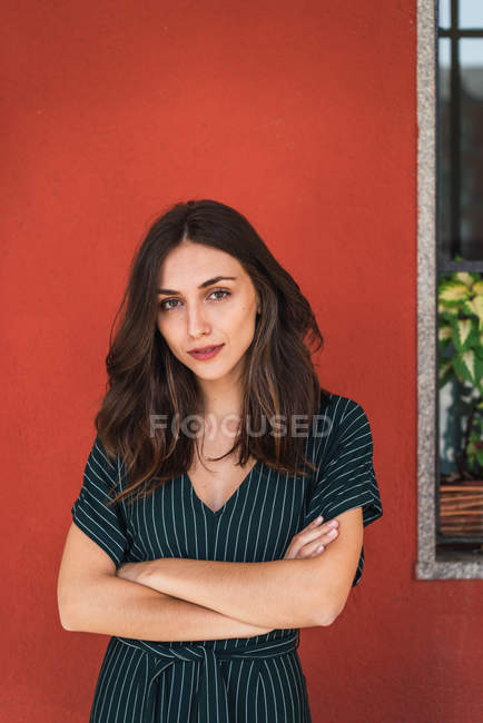 Cheerful brunette woman posing on red with arms crossed — Stock Photo