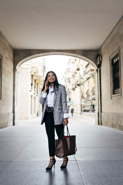 Elegante lächelnde Geschäftsfrau posiert mit Telefon auf dem Torbogen der Straße — Stockfoto