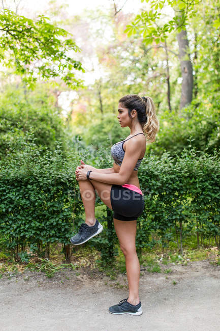 Девушка растягивает ногу перед пробежкой в парке — стоковое фото