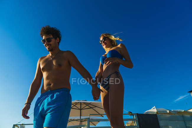 Vista ad alto angolo della coppia in occhiali da sole che cammina sulla spiaggia illuminata dal sole — Foto stock