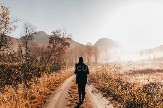 Voltar vista turista feminina andando na estrada rural no dia ensolarado de outono . — Fotografia de Stock