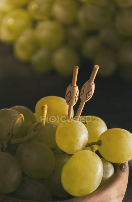 Vue rapprochée des raisins et des brochettes dans un bol en bois — Photo de stock