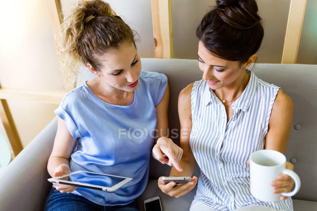Porträt zweier Geschäftsfrauen, die in der Kaffeepause auf Geräten surfen — Stockfoto