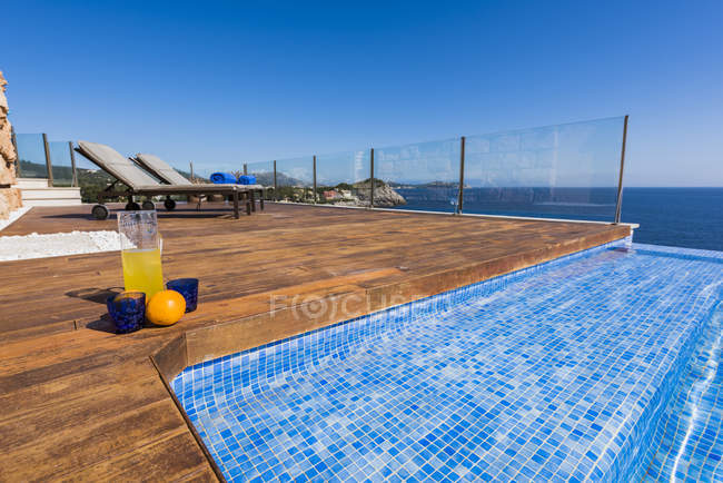 Vista exterior de la terraza de madera con tumbonas y agua azul en la piscina en el fondo - foto de stock