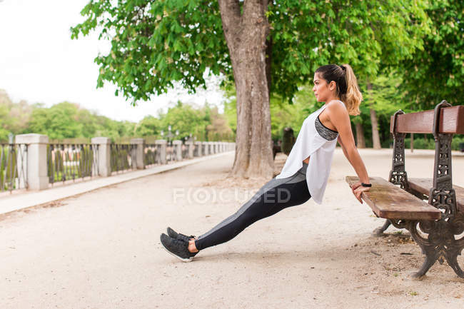Seitenansicht eines Mädchens, das sich mit den Händen auf eine Bank lehnt und den Körper hochstreckt — Stockfoto