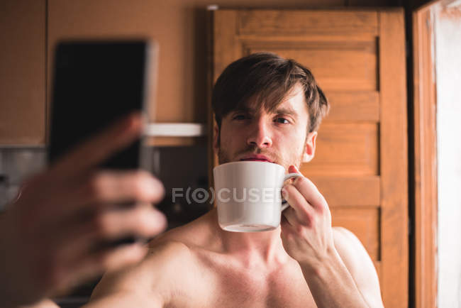 Homem com copo e selfie fazendo na cozinha . — Fotografia de Stock