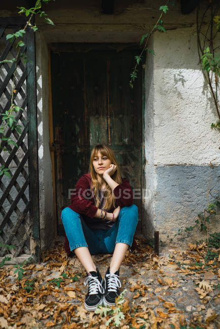 Portrait de fille brune portant un sweat à capuche assis sur le sol au trou de porte dans le parc et regardant loin — Photo de stock